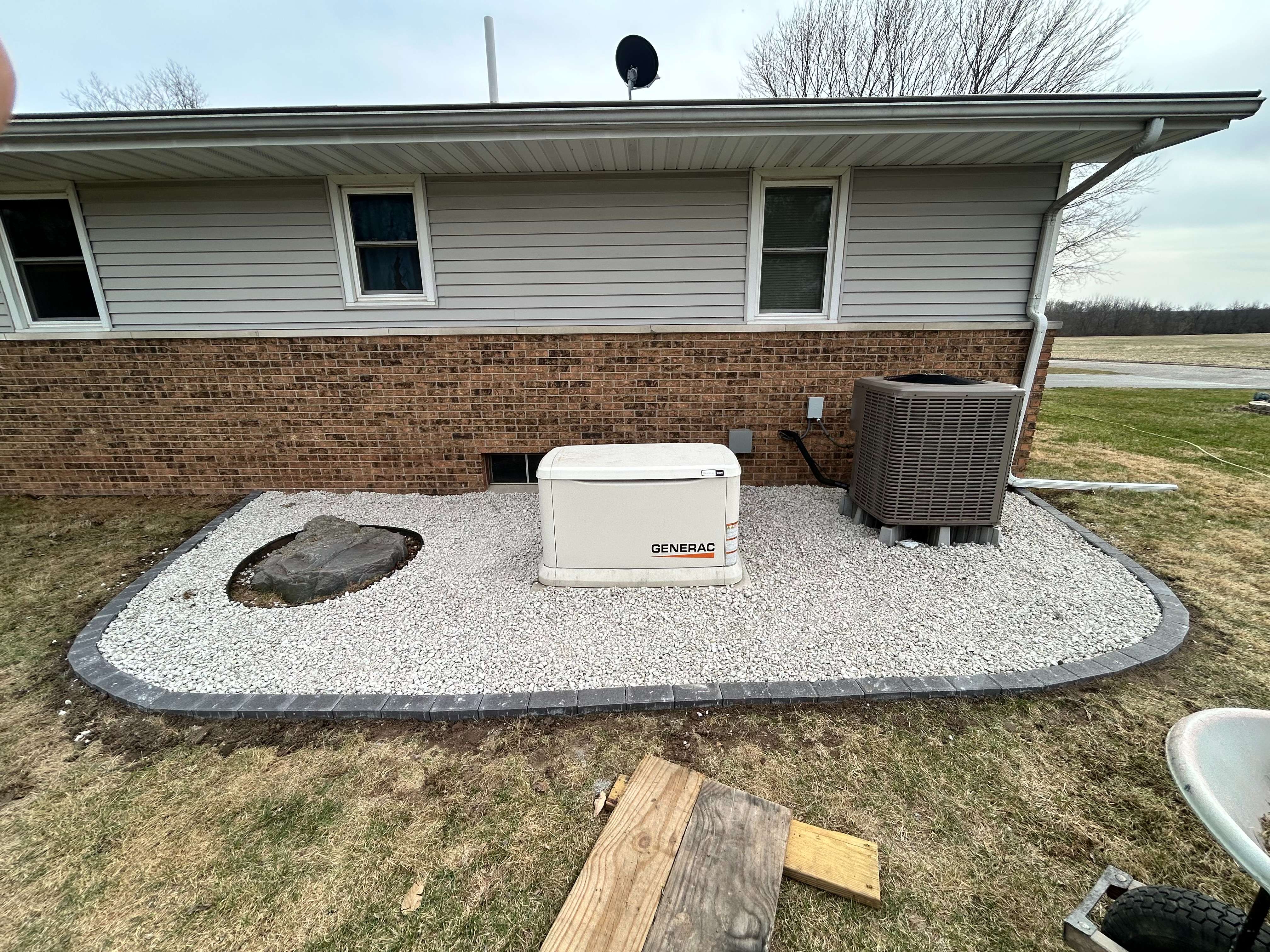 Generac home generator on gravel pad next to brick house and AC unit