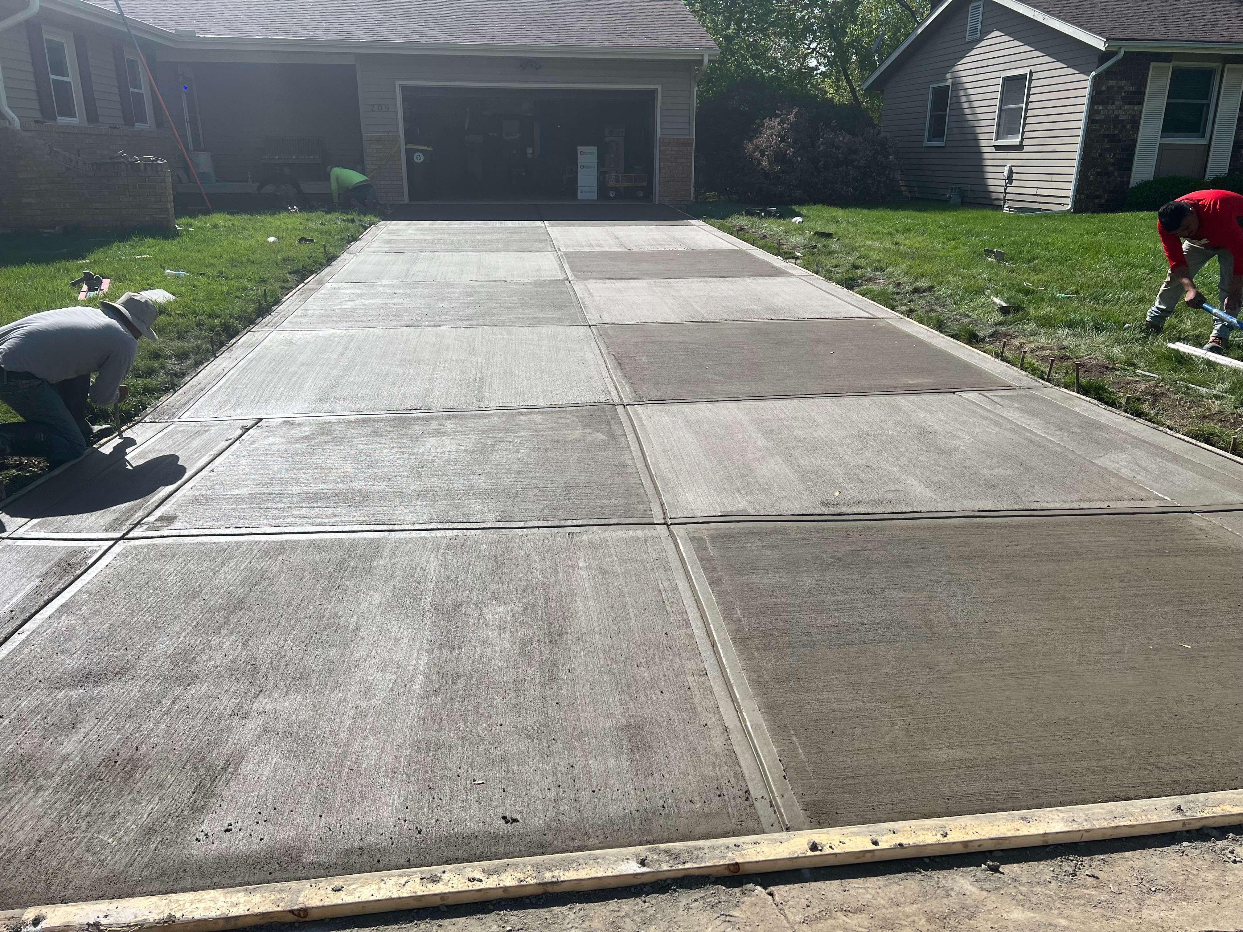 Workers finishing a newly poured concrete driveway in front of a suburban home