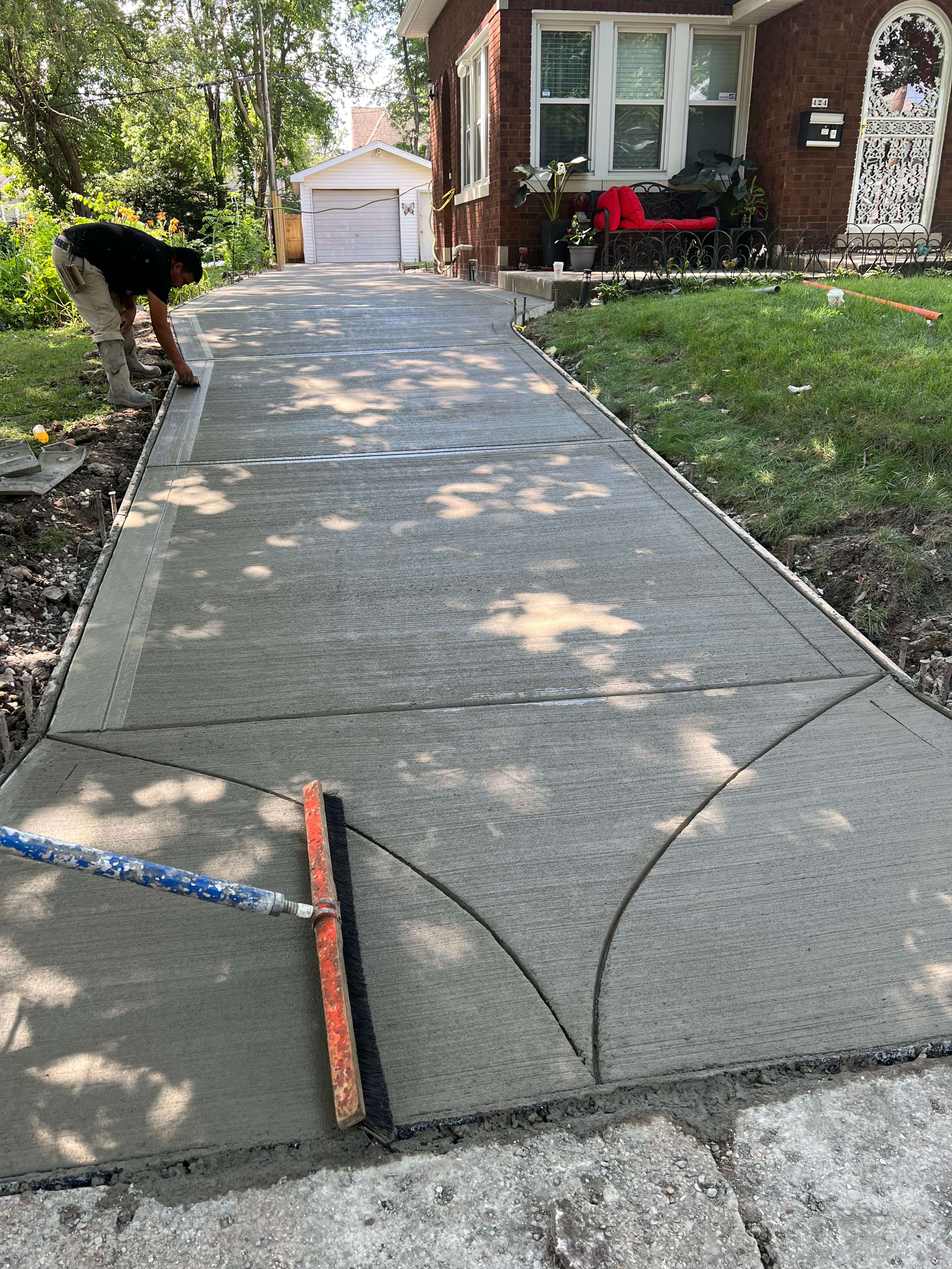 Fresh concrete sidewalk being smoothed with dappled sunlight through trees