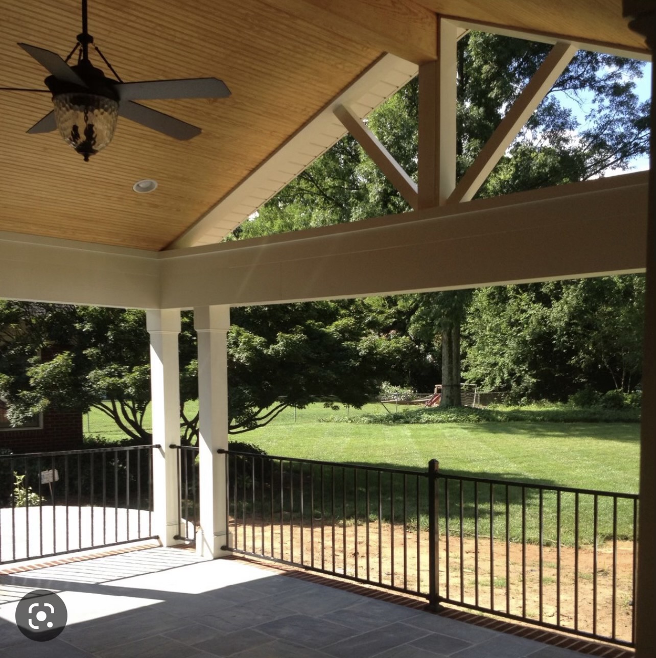 Covered porch with ceiling fan overlooking green backyard and trees