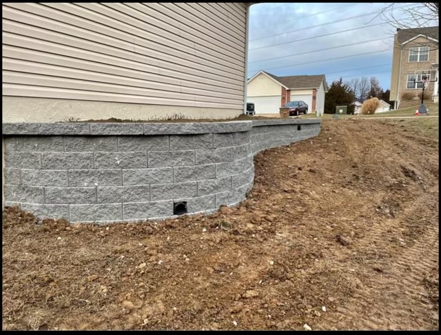 Gray retaining wall under house with exposed dirt and suburban background
