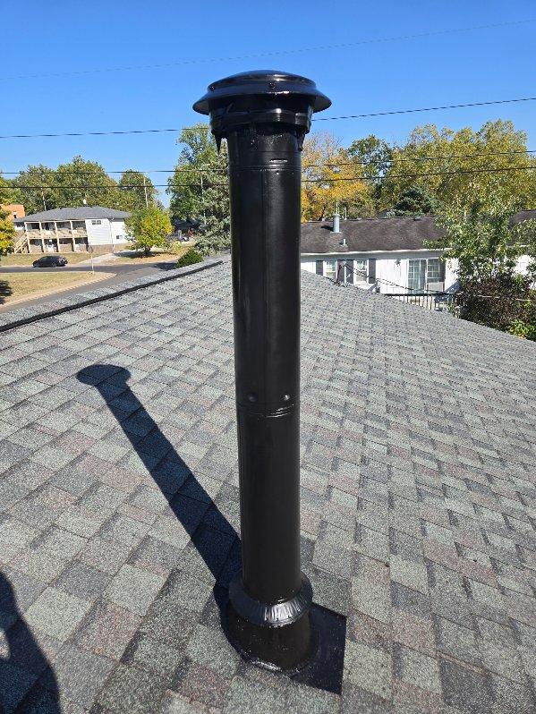 Black roof pipe vent on shingled roof with trees and houses in background